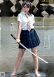 A woman in a school uniform holding a sword in the water.