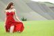 A woman in a red dress sitting in a green field.