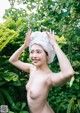 A naked woman with a towel on her head in the woods.