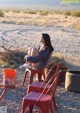 A woman sitting on a red chair in the desert.